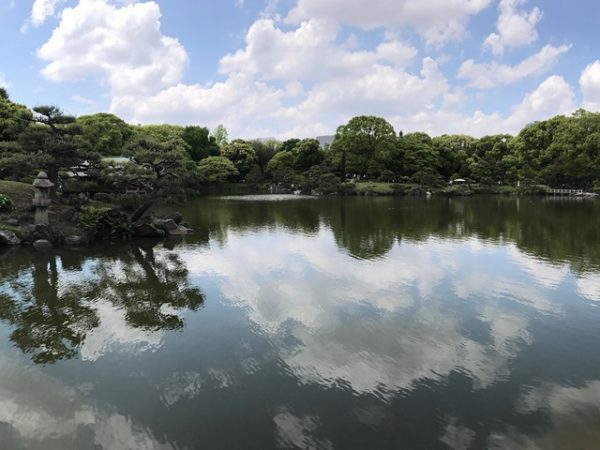 Metropolitan Gardens : 東京都故園, Japanese Culture, The lake at Kiyosumi gardens reflecting the sky and clouds above and the trees closer to the water’s edge.