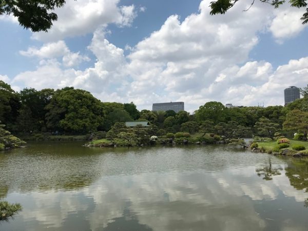 Metropolitan Gardens : 東京都故園, Japanese Culture, Sky reflected on the waters of the small lake at Kiyosumi gardens with trees and modern buildings in the background.