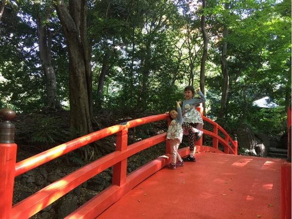 Metropolitan Gardens : 東京都故園, Japanese Culture, Vermillion wooden arch bridge, two little girls, green woods in the background, Japanese culture