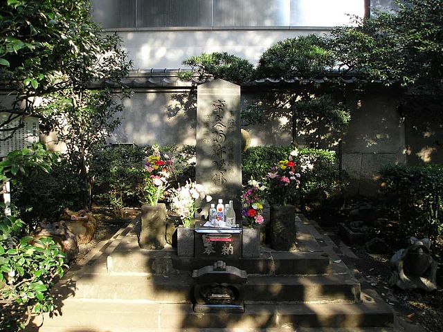 A small grave site with flowers and flanked by frog statues.