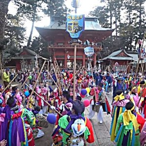 People in very colorful Japanese dress are standing in front of the great Kashima shrine with long poles.