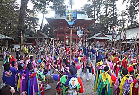 People in very colorful Japanese dress are standing in front of the great Kashima shrine with long poles.