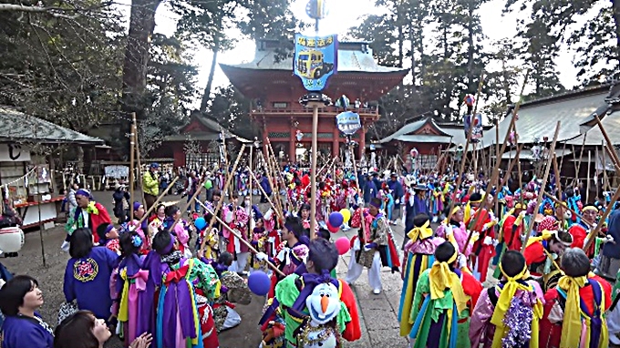 People in very colorful Japanese dress are standing in front of the great Kashima shrine with long poles.