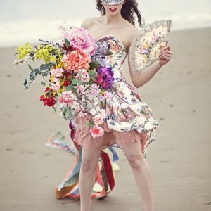 A young woman dressed with many flowers standing on a beach.