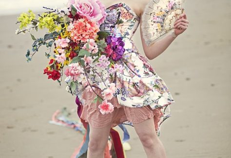 A young woman dressed with many flowers standing on a beach.