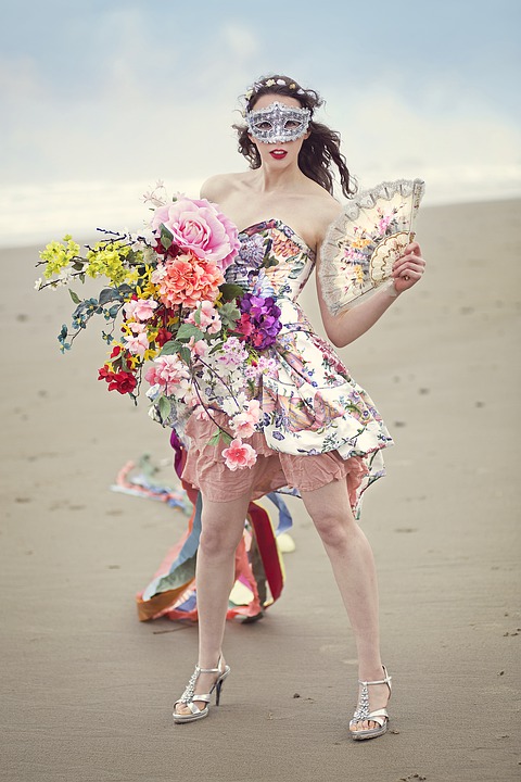 A young woman dressed with many flowers standing on a beach.