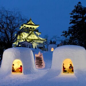 Exoteric Japan, Japanese Culture, two Kamakura, or Japanese snow huts lit from within on a winter night with Yokote castle in the background