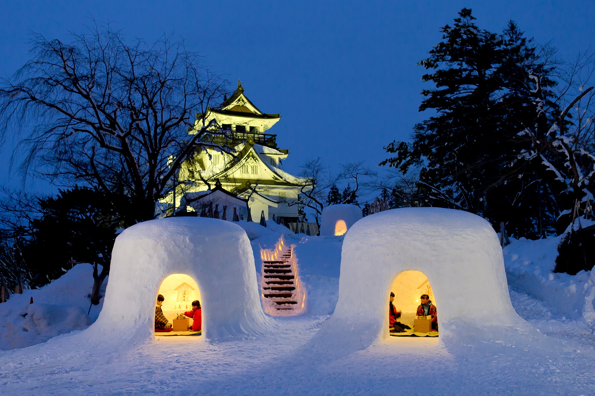 Exoteric Japan, Japanese Culture, two Kamakura, or Japanese snow huts lit from within on a winter night with Yokote castle in the background