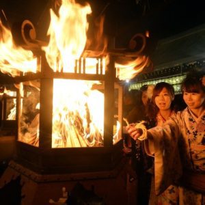 Two young women lighting a coil of rope at a lantern with a raging fire., December in Japan