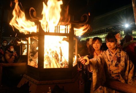 Two young women lighting a coil of rope at a lantern with a raging fire., December in Japan