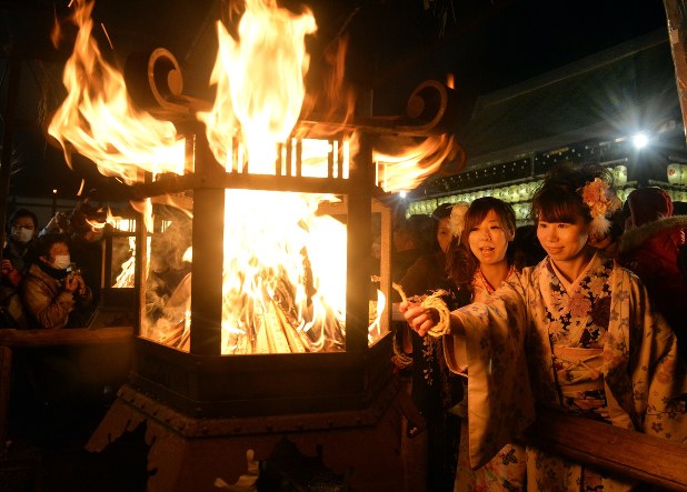 Two young women lighting a coil of rope at a lantern with a raging fire., December in Japan