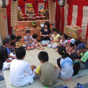 Japanese Culture, Jizō Bon, Children sitting in a circle and playing a game in front of Jizō statues.