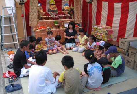 Japanese Culture, Jizō Bon, Children sitting in a circle and playing a game in front of Jizō statues.
