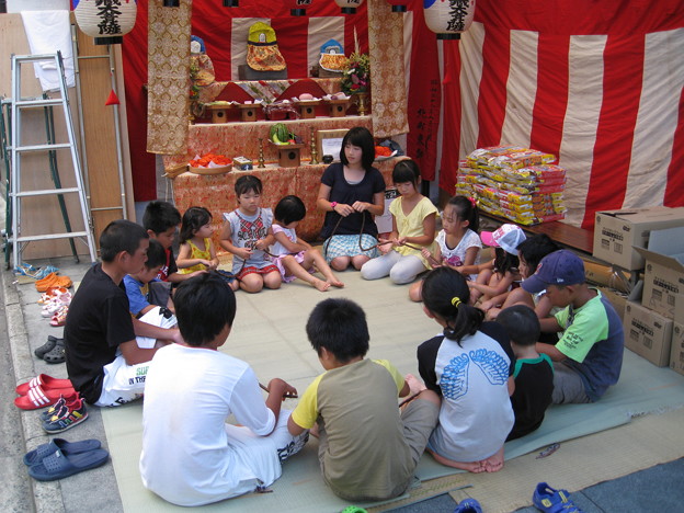 Japanese Culture, Jizō Bon, Children sitting in a circle and playing a game in front of Jizō statues.